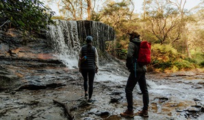 2 walkers on Grand Cliff Top Walk admiring the waterfall at Weeping Rock, Greater Blue Mountains Heritage Area. Photo: Remy Brand © Remy Brand
