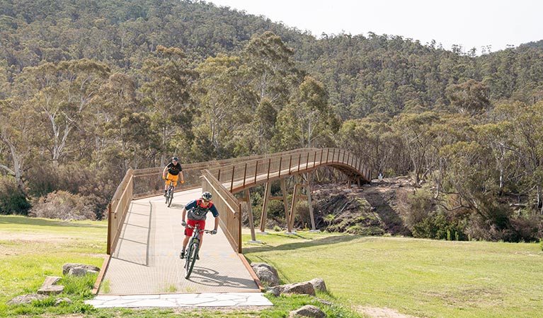 Two mountain bike riders cross a bridge from Thredbo Valley track, in Kosciuszko National Park, to Gaden Trout Hatchery. Photo: Robert Mulally/DPIE