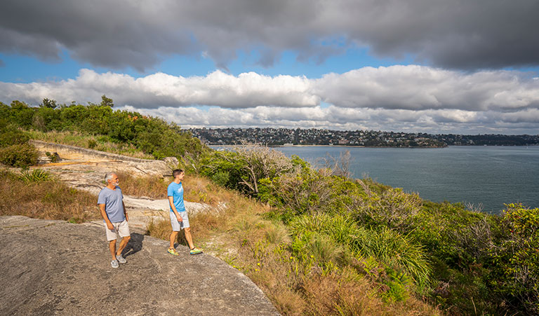 Two people walking along the rocks at Middle Head – Gubbuh Gubbuh in Sydney Harbour National Park. Photo: John Spencer, &copy; DCCEEW